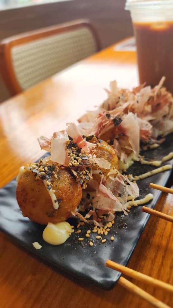 Takoyaki topped with dancing bonito flakes, sesame and mayo on a black plate.